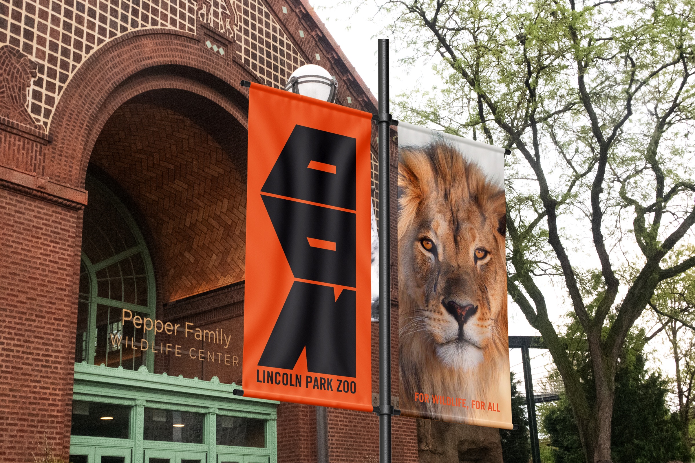 Orange ZOO banner and lion banner on a lamppost outside the zoo’s brick entrance